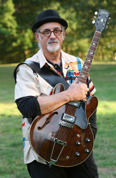 Larry Maltz outdoors holding a guitar