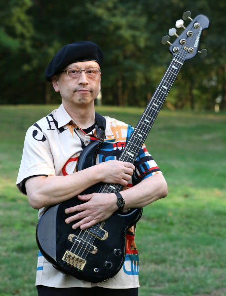 Takashi Otsuka outdoors holding a bass guitar